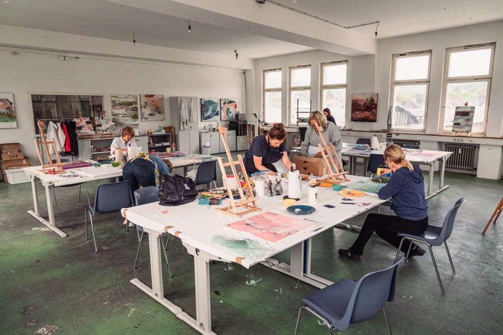 Art studio with several people working on their paintings at tables surrounded by natural light