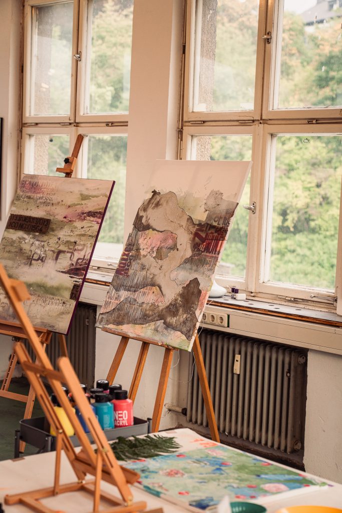 Art studio interior with two canvases on easels colorful abstract paintings and an outdoor view through the windows